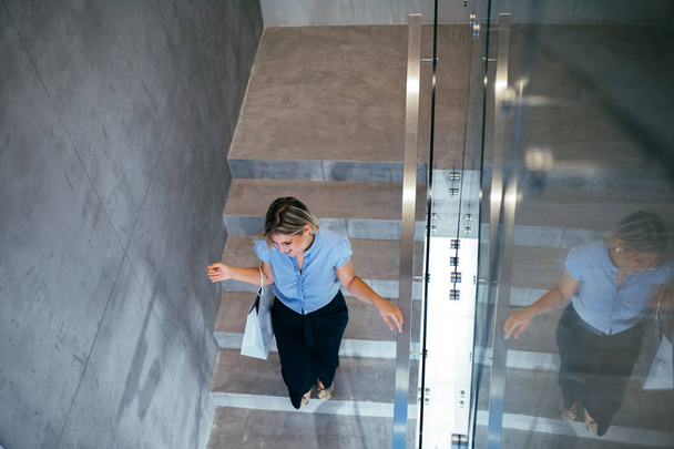 Shot from above of an attractive young woman walking down the stairs and carrying shopping bags. - Foto, Imagem