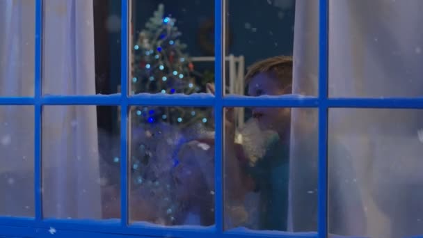 Dzieci i kobieta patrząc w okno przed świętami Bożego Narodzenia - Materiał filmowy, wideo