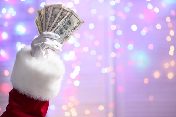 Main du Père Noël tenant des billets en dollars contre des lumières défocalisées
 - Photo, image