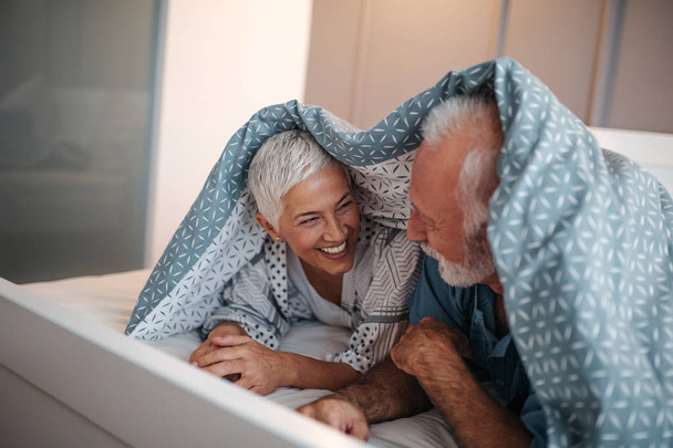 A happy senior couple being silly in bed on a beautiful sunny morning. - Foto, afbeelding
