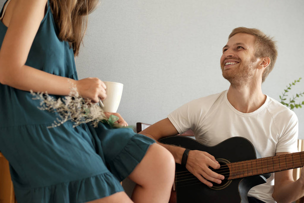 Carismatico giovane uomo che suona la chitarra per la sua ragazza a casa
 - Foto, immagini