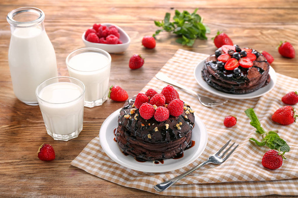 Teller mit leckeren Schokoladenpfannkuchen, Beeren und Milch auf Holztisch - Foto, Bild