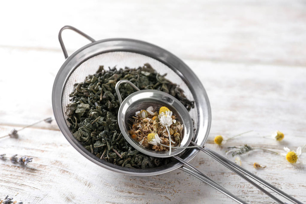 Tamices con manzanilla seca y hojas de té sobre mesa de madera blanca
 - Foto, Imagen