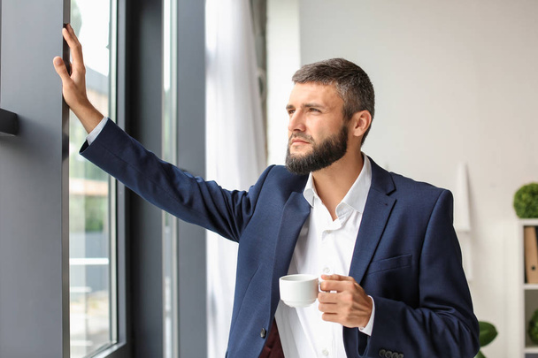 Businessman drinking coffee near window in office - Фото, изображение