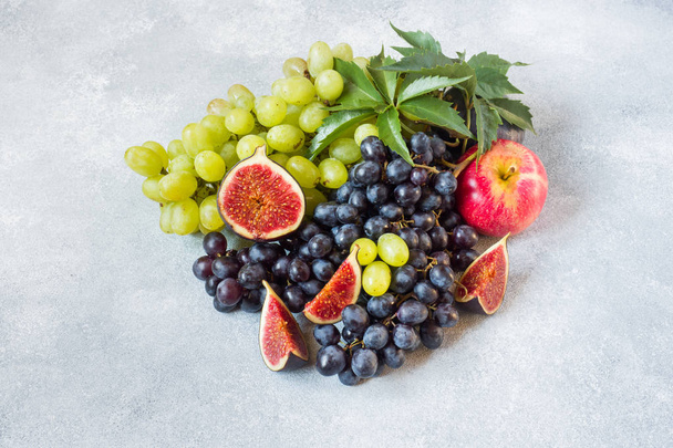 Still life of fresh autumn fruit. Grapes black and green, figs and leaves on a grey table with copy space - Photo, image