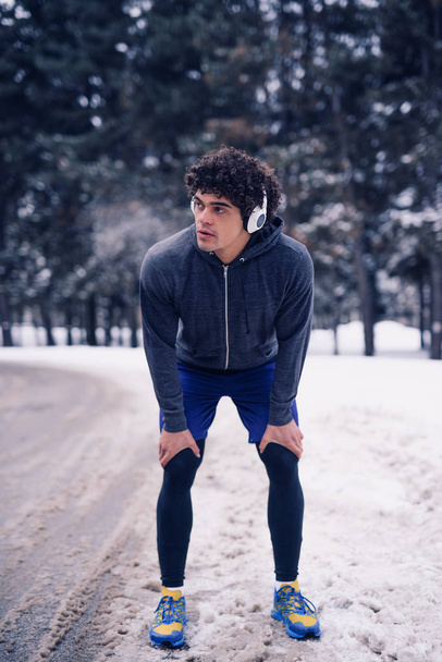 Athlete man listening to the music while working out in the winter outdoors. - Zdjęcie, obraz