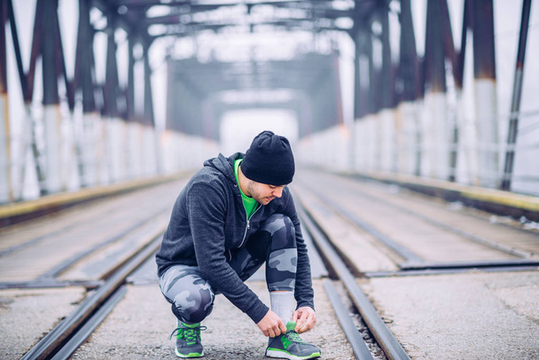 Athlete man trying shoes on the bridge. - Photo, Image