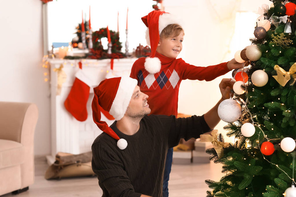 Cute boy with father decorating Christmas tree in room - Zdjęcie, obraz