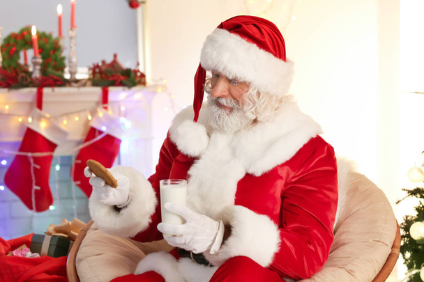 Santa Claus with cookie and glass of milk in room decorated for Christmas - Foto, Imagen
