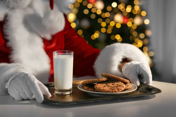 Santa Claus eating cookies and drinking milk at table, closeup - Фото, изображение