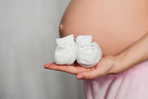 botines para recién nacidos en las manos de una chica embarazada en el fondo del abdomen
 - Foto, imagen