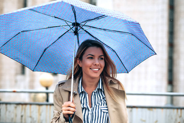 Smiling young woman holding an umbrella outdoors. - Zdjęcie, obraz