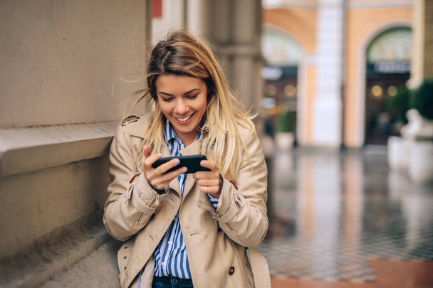 A young beautiful woman using her phone on a cold autumn day. - 写真・画像