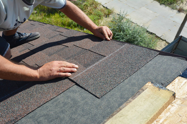Dakdekker asfalt gordelroos installeren op huis bouw dak hoek. Bouw van de dakbedekking. Dakdekker installeren dakpannen. - Foto, afbeelding