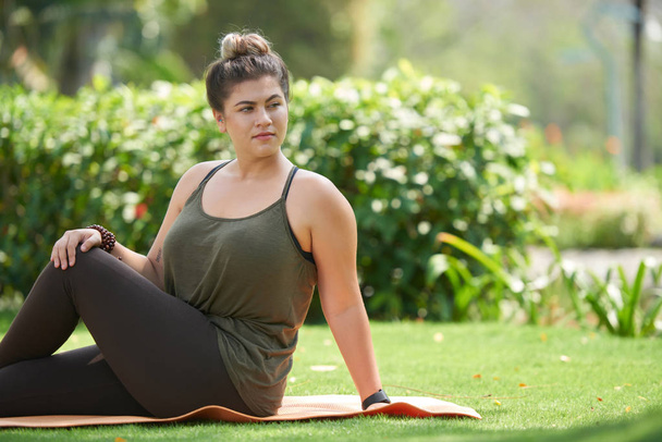 Mujer bastante joven en ropa deportiva sentada en una esterilla de yoga y haciendo ejercicio de estiramiento
 - Foto, imagen