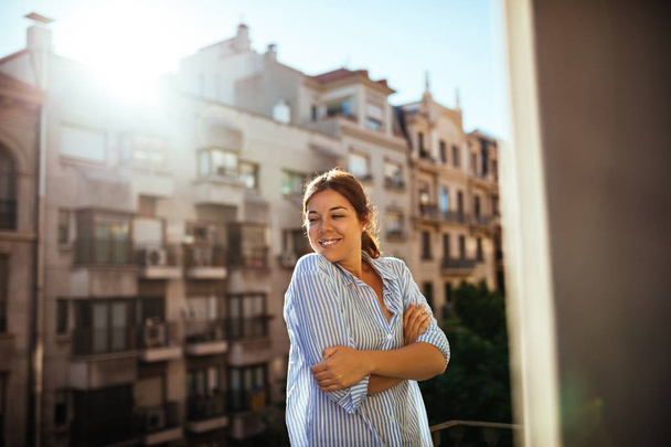 Beautiful woman standing on a balcony and enjoying morning sun. - Photo, image