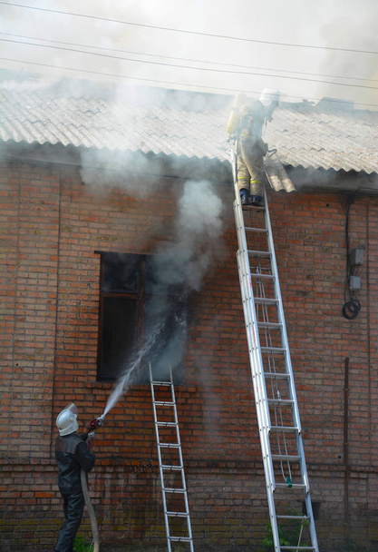 Brandende huis en brandweerlieden op de ladders. - Foto, afbeelding