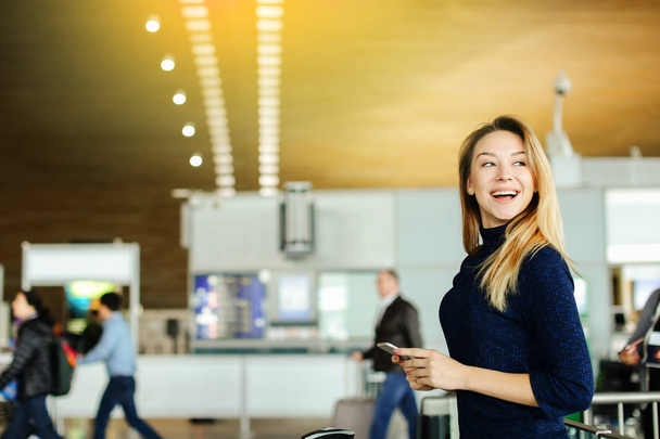 Молода жінка тримає смартфон в залі очікування аеропорту, з копіювальним простором
. - Фото, зображення