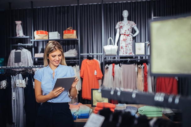 Beautiful woman using digital tablet in a clothing store. - Fotografie, Obrázek