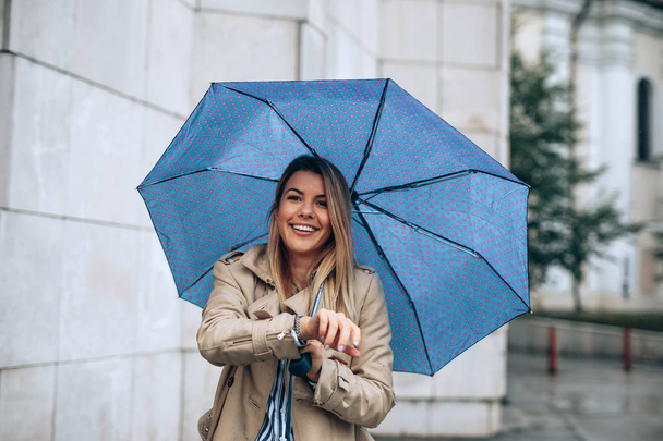 Młoda kobieta zadowolony czekając na kogoś wyjątkowego pod jej niebieski parasol. - Zdjęcie, obraz
