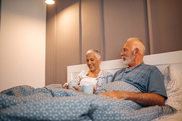 A senior couple enjoying a morning coffee together in bed. - Photo, image