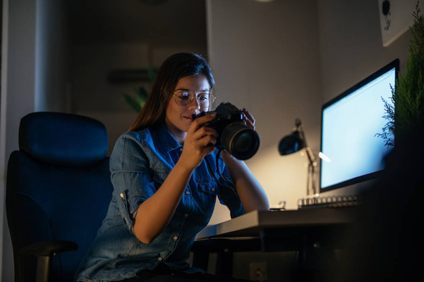 Giovane fotografa che guarda la sua macchina fotografica e lavora di notte
. - Foto, immagini