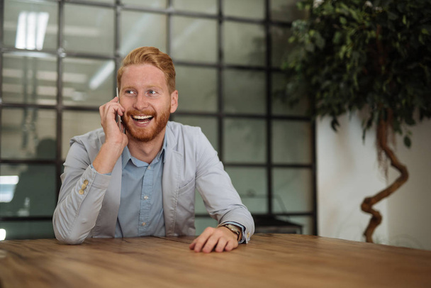 Retrato de un joven hombre de negocios sonriente hablando por teléfono en el interior
. - Foto, Imagen