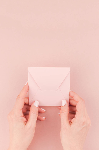 Creative image of woman hand holding small love letter with copy space on millennial pink background in minimalism style. Concept template for feminine blog, social media - Foto, Bild
