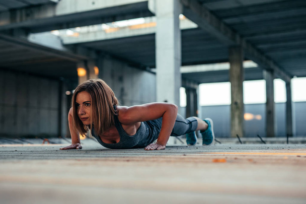Schot van een vastberaden atleet vrouw doet push ups in een verlaten gebouw. - Foto, afbeelding