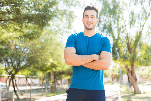 Portret uśmiechający się młodego sportowca, stojąc z rękami po złożeniu w parku - Zdjęcie, obraz