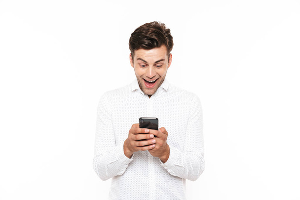 Happy young man with short dark hair chatting or typing text message with smartphone isolated over white background - Foto, imagen