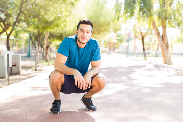 Full length portrait of confident young man taking break after running in park on sunny day - Photo, Image