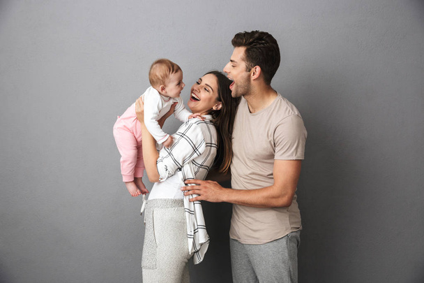 Portrait of a cheerful young family with their little baby girl isolated over gray background - 写真・画像
