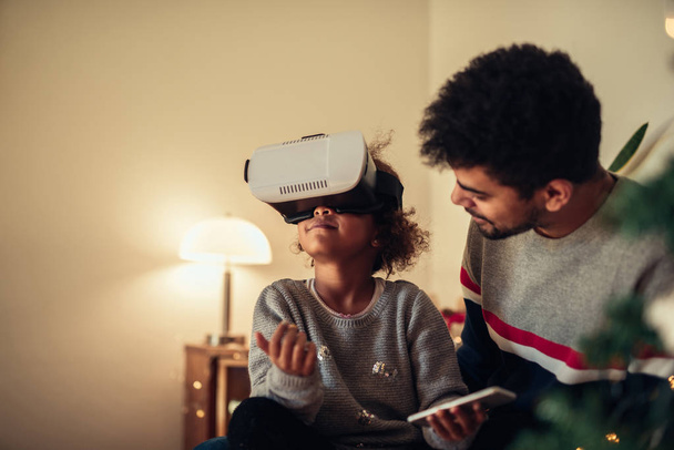 African american father and daughter enjoying using virtual reality headset at home. - Foto, afbeelding