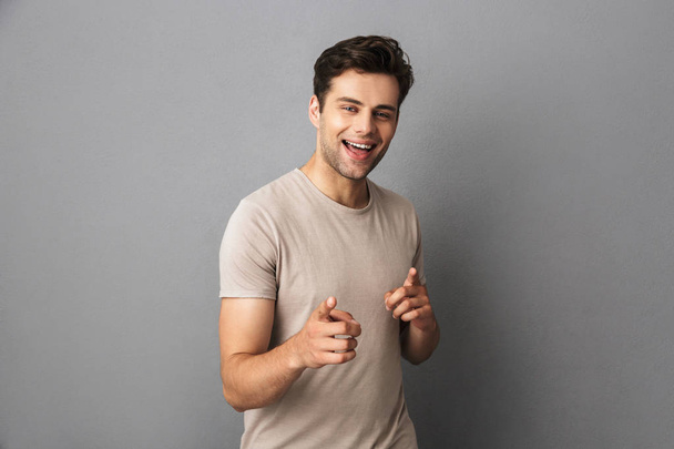 Image of handsome guy 30s having stubble pointing fingers at camera like hey you isolated over gray background - Fotografie, Obrázek
