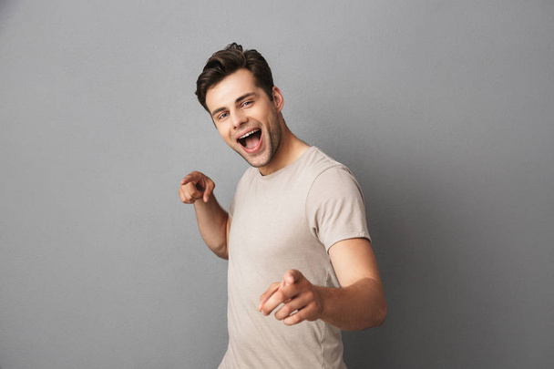 Image of optimistic brunette guy 30s pointing fingers at camera like hey you isolated over gray background - Φωτογραφία, εικόνα