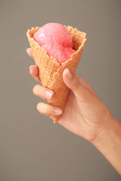 Nő gazdaság waffle kúp finom eper fagylaltot a szürke háttér - Fotó, kép