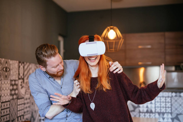 Attractive young couple enjoying using virtual reality headset at home. - Foto, Bild