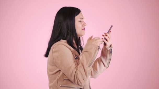 Angry modern businesswoman screaming down her mobile phone in slow motion. Stressed and depressed girl on pink background - 映像、動画