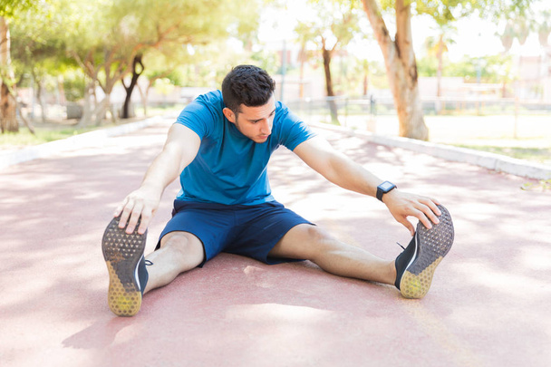volle Länge des flexiblen sportlichen Mannes, der beim Aufwärmen auf der Laufstrecke im Park die Zehen berührt - Foto, Bild