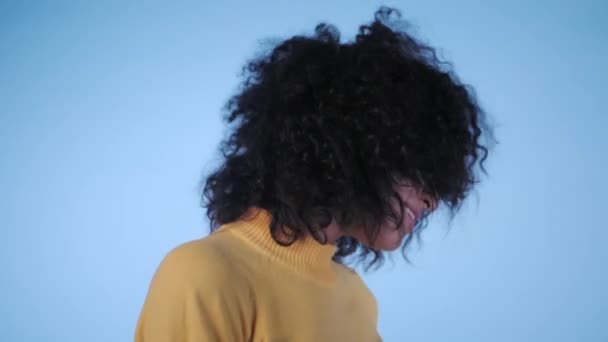 beautiful black woman with afro hair having fun smiling and dancing in studio against blue background. slow motion. - Záběry, video