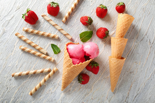 Cônes de gaufre avec délicieuse crème glacée aux fraises et bâtonnets sur fond en bois
 - Photo, image