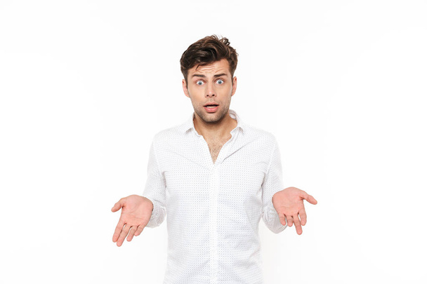 Portrait of a confused young man in shirt isolated over white backgound, shrugging shoulders - Foto, Bild