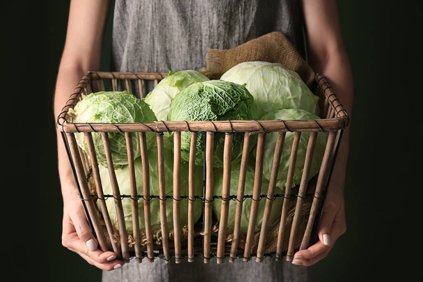 Woman holding basket with fresh cabbage on dark background - 写真・画像