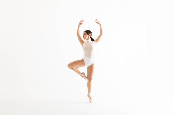 Pełna długość młodych balerina próby na jednej nodze z rękoma wzniesionymi na białym tle - Zdjęcie, obraz