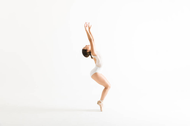 Täyspitkä sivukuva nuorten ballerina kädet nostetaan tasapainotus hänen varpaillaan valkoisella pohjalla
 - Valokuva, kuva