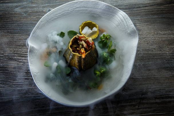 top view on dessert served in pumpkin decorated with fresh mint and smoke on restaurant plate on wooden table background - Foto, Imagem