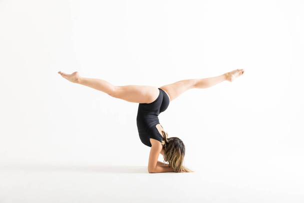 Volledige lengte van vrouwelijke balletdanser doet handstand met benen in split positie op witte achtergrond - Foto, afbeelding