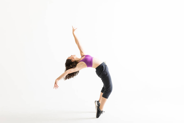 Vista lateral de cuerpo entero de una joven bailarina de jazz de puntillas inclinándose hacia atrás sobre fondo blanco
 - Foto, Imagen
