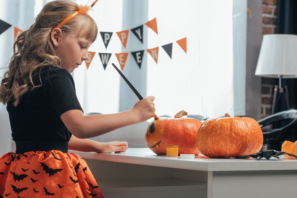 vista lateral de niños enfocados pintando calabazas para Halloween en casa
 - Foto, imagen